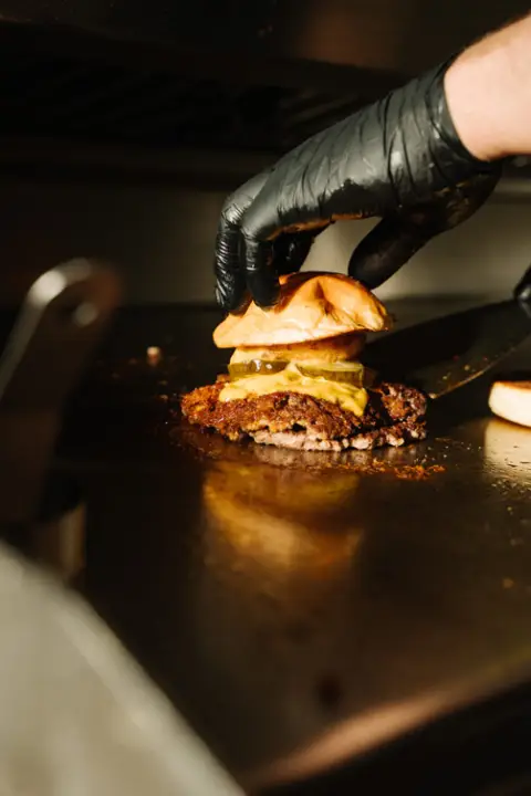 Burger mit geschmolzenem Käse über offener Flamme auf dem Grill