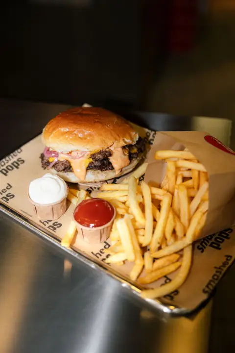 Smashed-Pops-Burger mit Fritten und Dips in der Pappschale