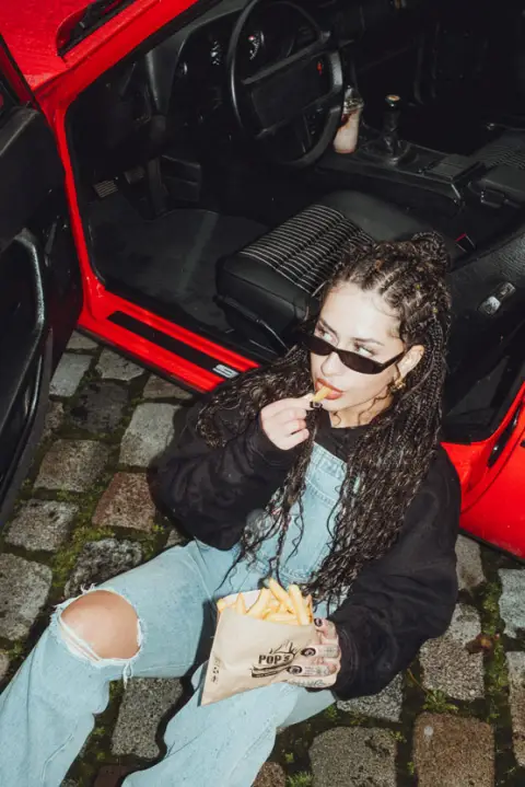 Gast mit POPs-Burger-Tüte an einem roten Auto